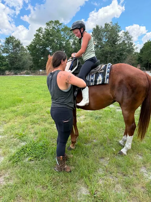 A Tree House Farm camper receiving hands-on help before riding